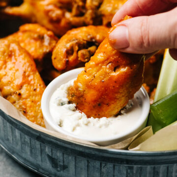 A woman's hand dipping a buffalo wing into a bowl of blue cheese dressing.