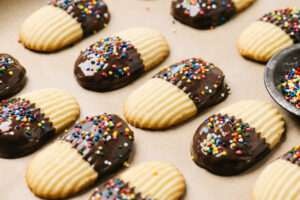 Chocolate dipped butter cookies with sprinkles on a parchment lined baking sheet.