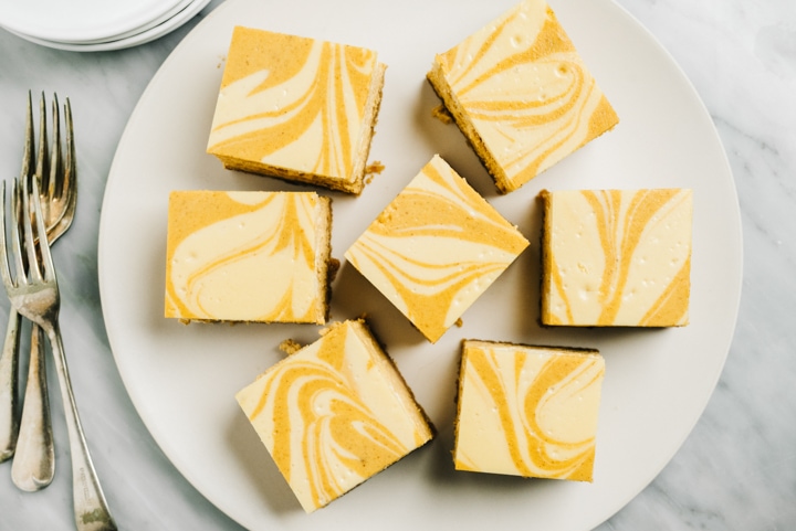 Pumpkin cheese cake bars cut into squares and arranged on a platter with silver forks and small plates on the side.