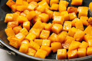 Roasted butternut squash cubes tossed with bacon fat in a skillet.