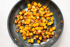 Roasted butternut squash with diced cooked bacon in a skillet.