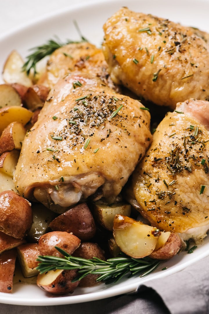 Sheet pan rosemary chicken and potatoes arranged on a white platter with a grey linen napkin.