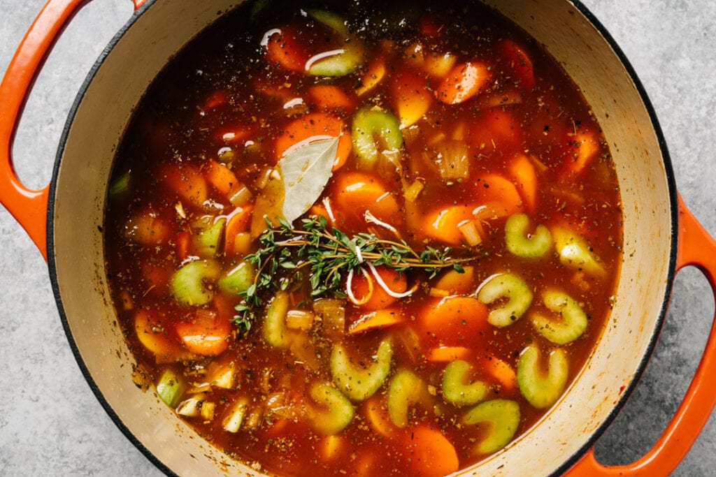 Vegetables simmering in a savory stew gravy topped with fresh thyme and a bay leaf.