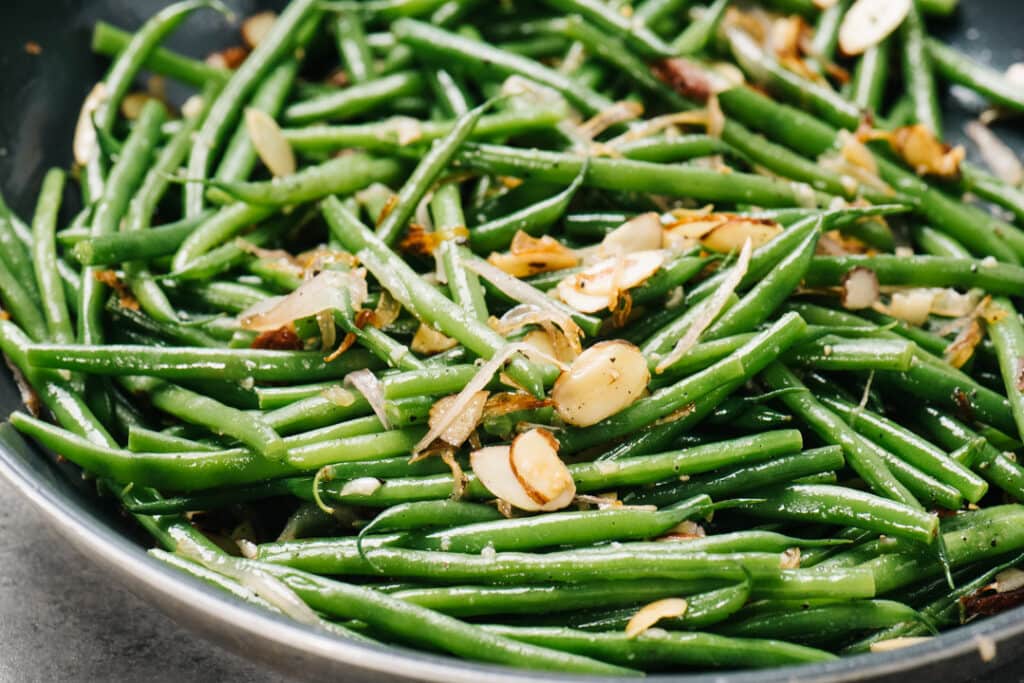 Tossing green beans with sauteed almond and shallots in a skillet.