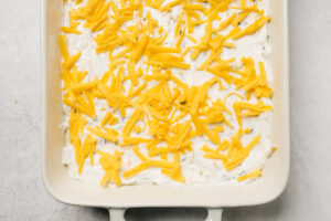 Unbaked jalapeno popper dip topped with shredded cheddar cheese in a casserole dish.