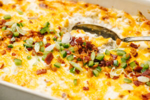 Side view, a serving spoon tucked into jalapeno popper dip garnished with chopped bacon, green onions, and minced fresh jalapenos.