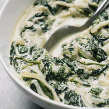Side view, keto creamed spinach in a white bowl with a silver serving spoon.