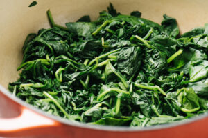 Wilted fresh spinach in a red dutch oven.