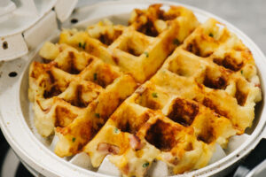 A mashed potato waffle with bacon and chives in a waffle iron.