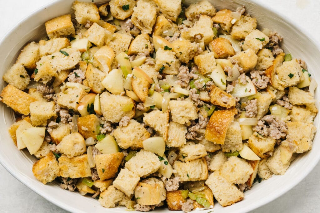 Uncooked sausage stuffing in a white oval casserole dish.