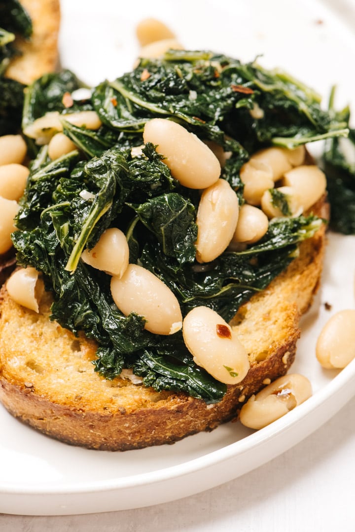 A serving of beans and greens on a piece of garlic toast on a white plate.