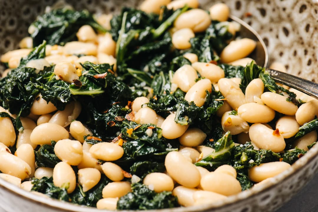 Side view, vegan beans and greens in a tan speckled serving bowl.
