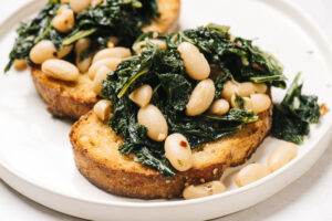 Side view, beans and greens served over garlic toast on a white plate.