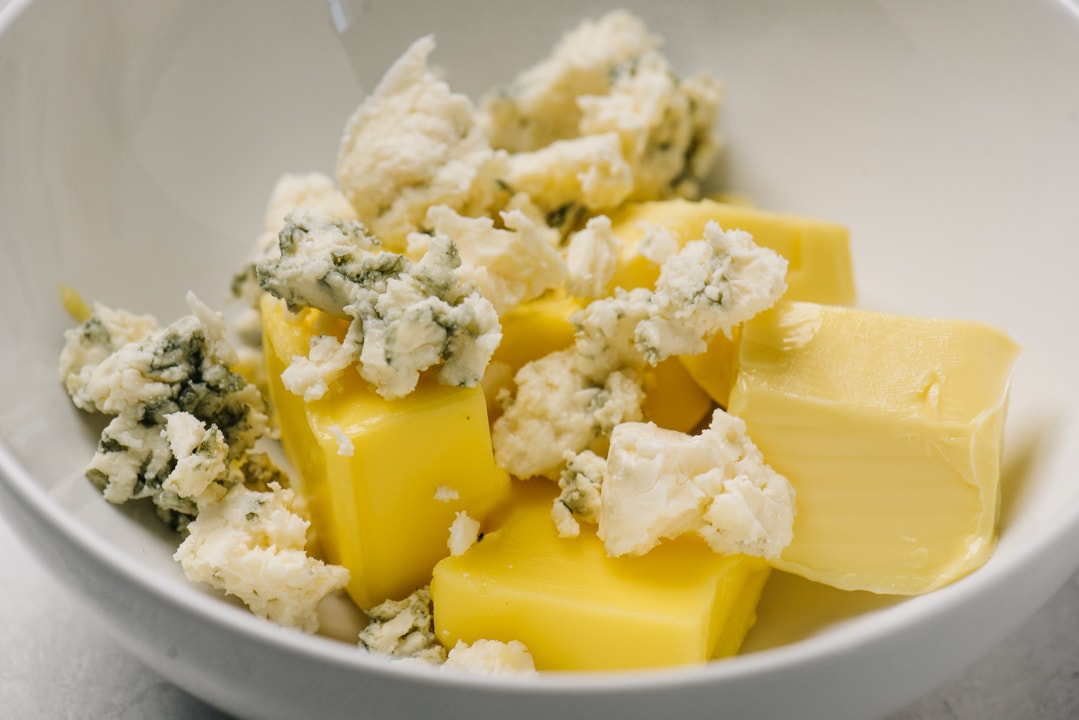 Slices of softened butter and chunks of blue cheese in a white bowl.