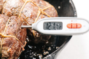 A digital thermometer inserted into a beef tenderloin roast registering a temperature of 121°F.