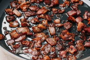 Chopped bacon crisping in a skillet.