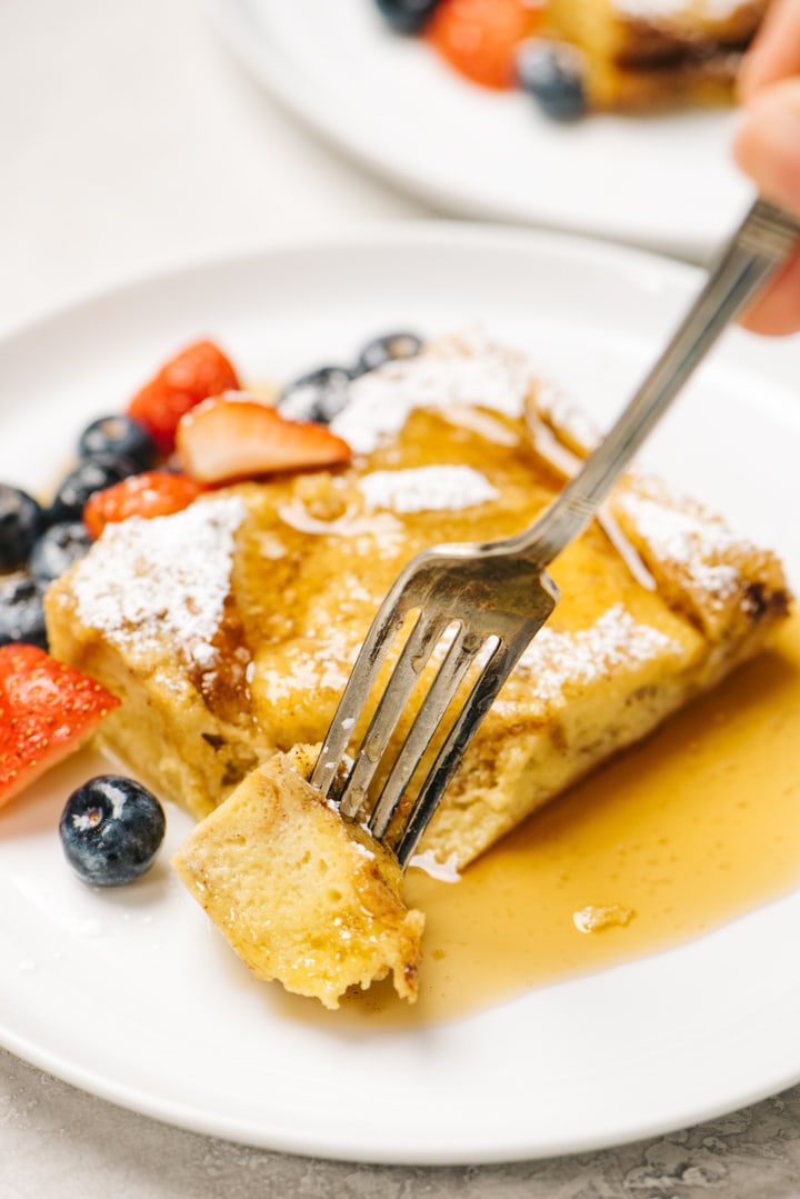 A woman's hand taking a bite of french toast casserole with a vintage silver fork.