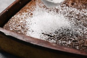Dusting powdered sugar over a cooled gingerbread cake.