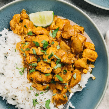 Instant pot chicken curry over white rice on a blue plate, garnished with cilantro and a lime wedge.