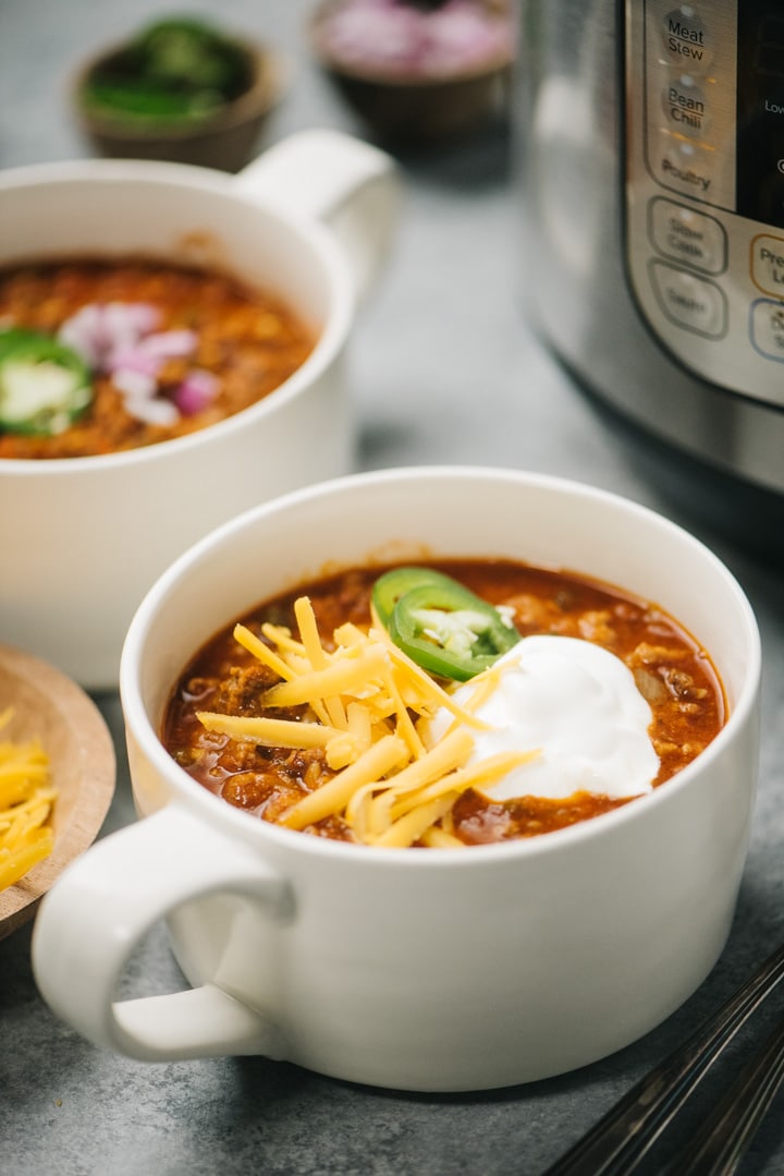 Two bowls of instant pot chili with a pressure cooker and small garnish bowls in the background.