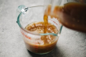 Combining beef broth and beef drippings in a 1-cup glass measuring cup.