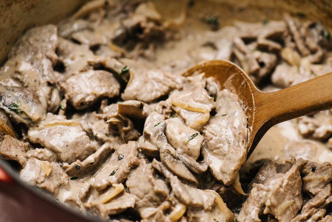 A wood spoon stirring keto beef stroganoff in a red dutch oven.