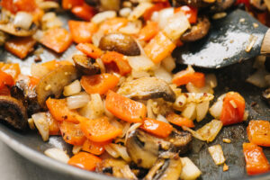 Sautéed onion, bell pepper, and mushrooms in a skillet.