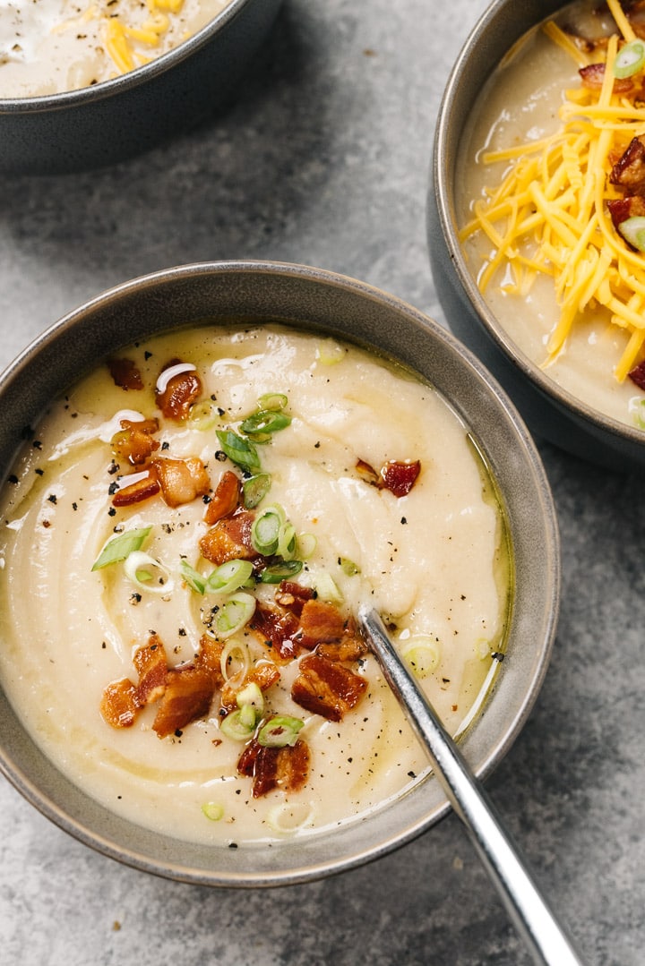 Three bowls of low carb and whole30 cauliflower soup with various garnishes, including cheese, bacon, and sliced green onions.