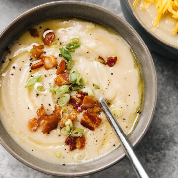 A bowl of loaded cauliflower soup garnished with bacon and sliced green onions.