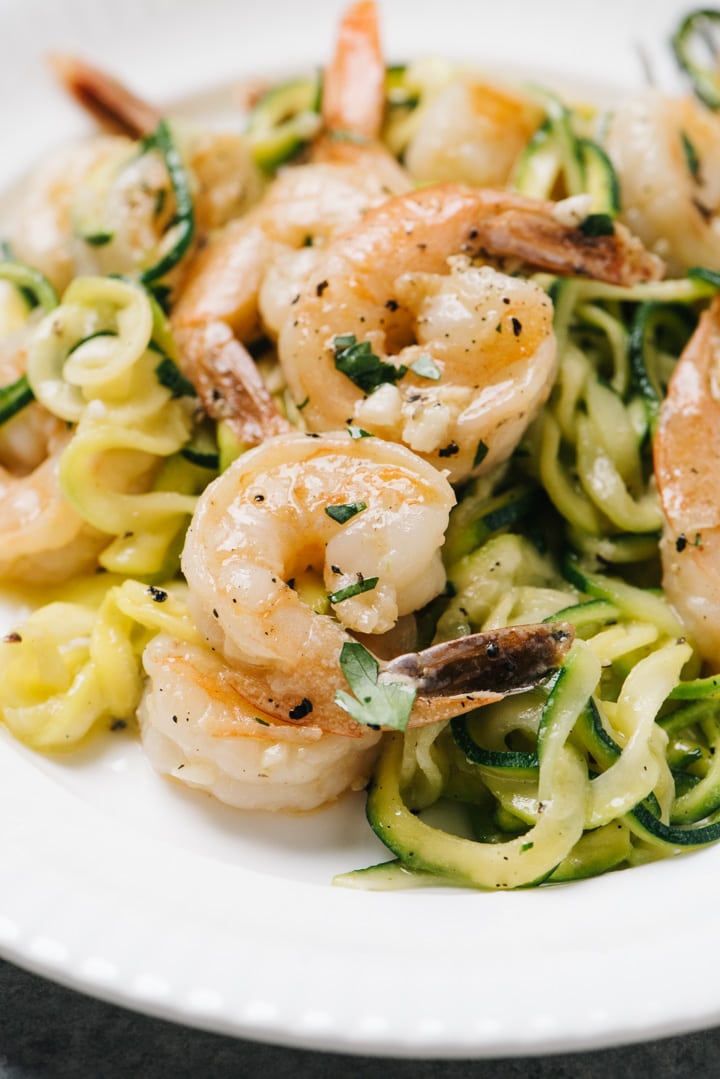 Side view, keto shrimp scampi tossed with zucchini noodles on a white plate.
