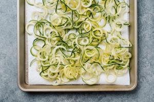 Zucchini noodles sweating on a paper towel lined baking sheet.