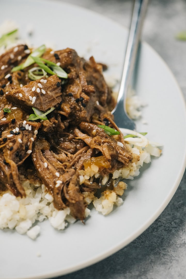 Side view, a silver fork tucked into a plate of korean beef served over cauliflower rice.