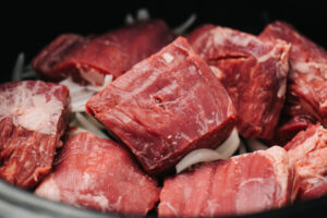 Sliced onions and chunks of flank steak in a slow cooker.