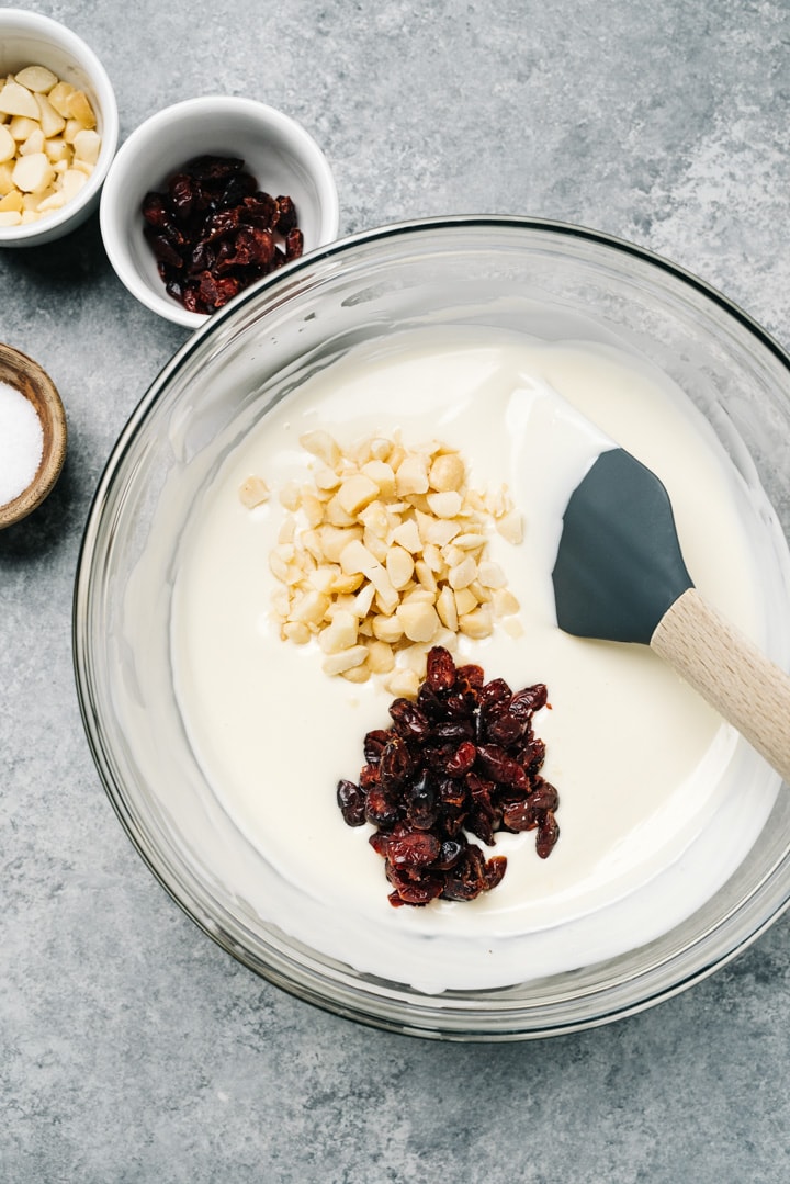 A glass bowl filled with melted white chocolate, macadamia nuts, and dried cranberries.