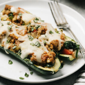 Two italian sausage zucchini boats on a white plate with a silver fork.