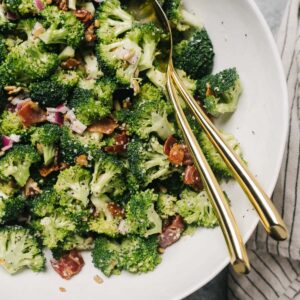 Keto broccoli salad with bacon and creamy poppy dressing in a white serving bowl on a concrete table with a striped linen napkin.
