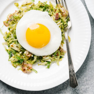 Brussels sprouts hash on a white plate topped with a fried egg, with a silver vintage fork.