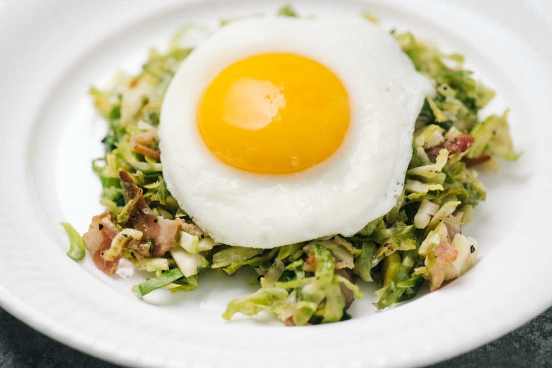 Side view, brussels sprouts hash on a white plate topped with a fried egg.