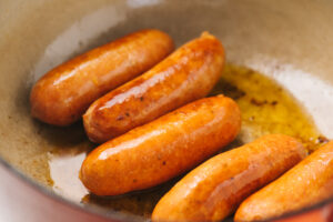 Chorizo sausage links browning in olive oil in a dutch oven.