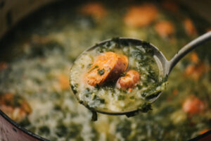 A ladleful of caldo verde hovering over a soup pot.
