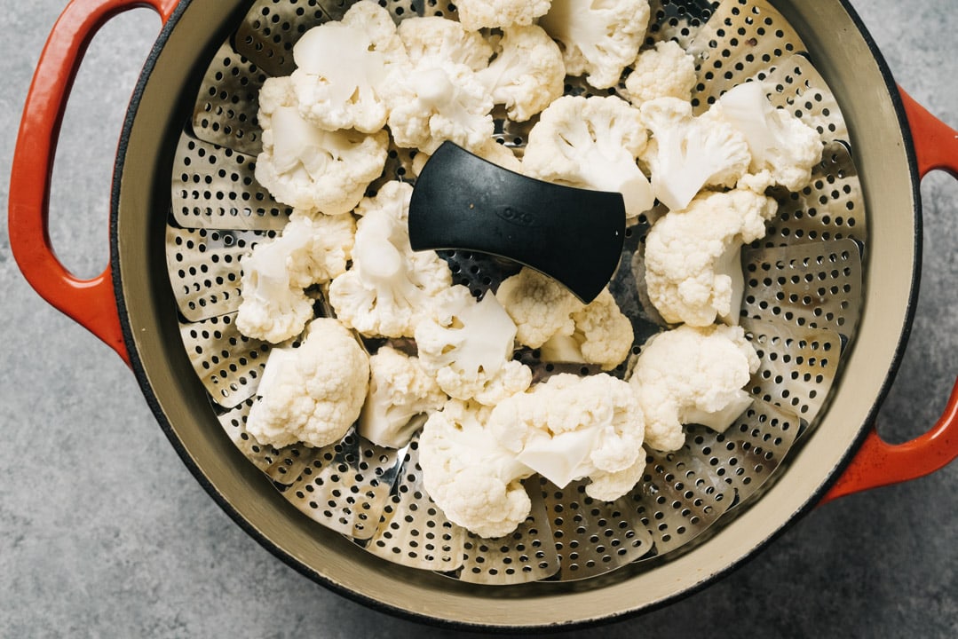 Cauliflower florets in a steamed basket nested in a dutch oven.