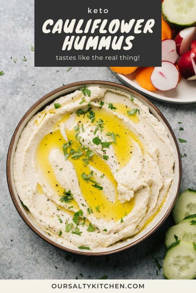 A bowl of cauliflower hummus dip on a cement background, surrounded by plates of sliced vegetables; title bar the top reads "keto cauliflower hummus - tastes like the real thing!".