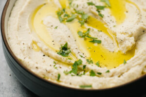Cauliflower hummus in a black bowl, garnished with olive oil, chopped parsley, and pepper.