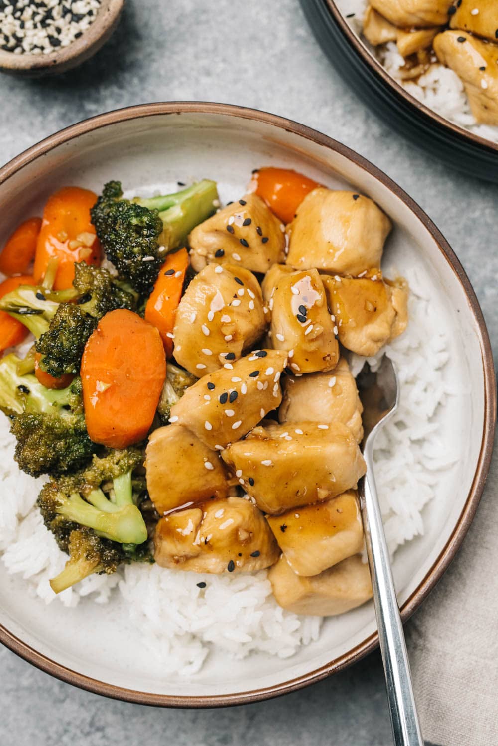 A healthy chicken teriyaki bowl with rice, chicken, broccoli, and carrots on a concrete background.