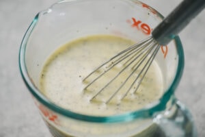 Creamy keto poppy dressing in a 1 cup measuring cup with a whisk.