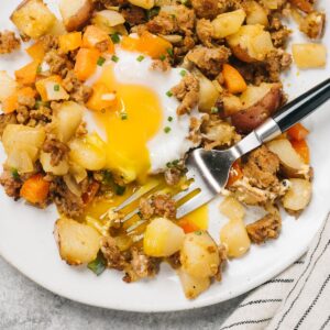 A serving of mexican potato hash on a white plate with a fork breaking the egg yolk.