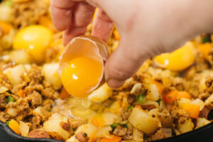 Adding an egg to potato hash to make it a complete meal.
