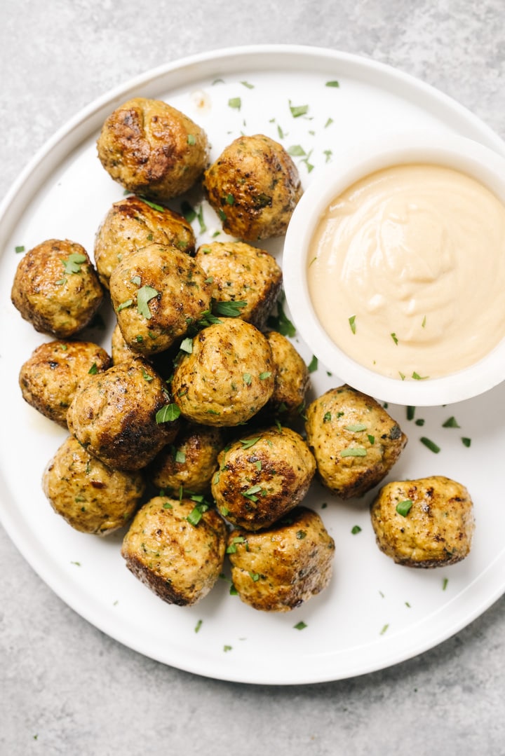 Keto chicken meatballs on a white platter with a small bowl of tahini dipping sauce.