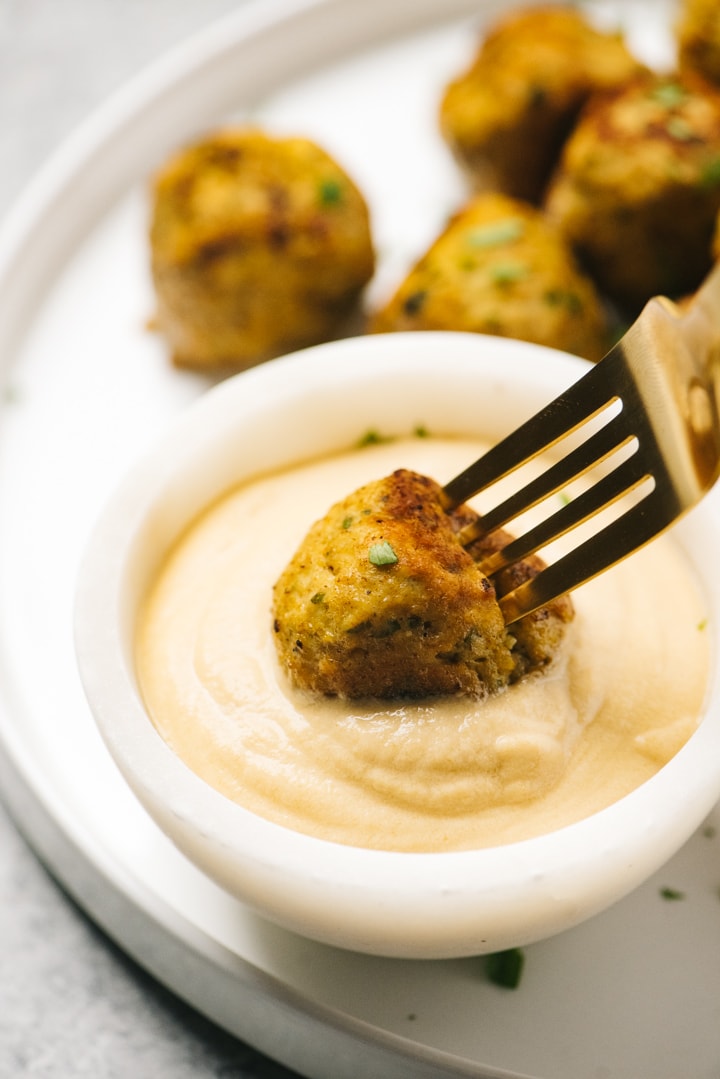 A gold fork dippin a keto chicken shawarma meatball into a small bowl of tahini dressing.