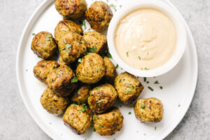 Chicken shawarma meatballs on a white platter with a small bowl of tahini dipping sauce.